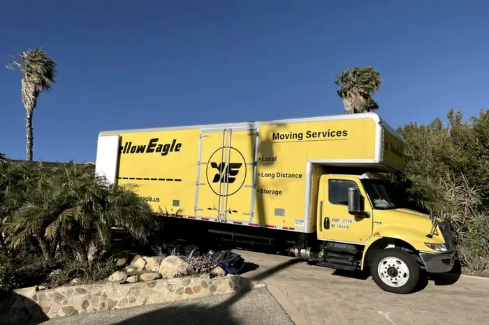 A yellow Yellow Eagle box truck parked on a driveway between palms