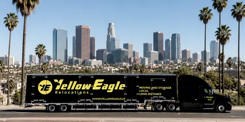 A Yellow Eagle tractor and trailer, side on, before a city skyline and palms