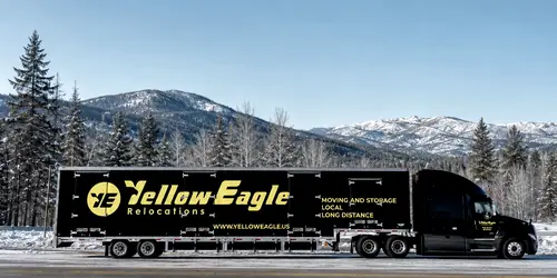 A Yellow Eagle tractor and trailer, side on, before snow-covered mountains
